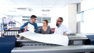 Three people looking at a roll of plotter paper.