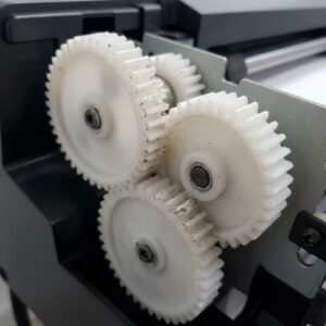 worn and chipped white plastic gears within a wide-format plotter printer's drive assembly