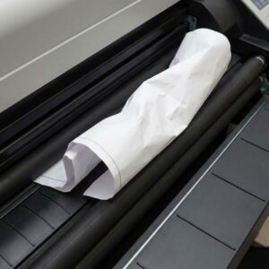 A piece of crumpled blueprint paper causing a severe paper jam and obstruction inside the feed rollers of a professional plotter printer